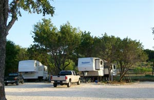 Fifth-wheel trailers and pickups on gravel sites under the trees